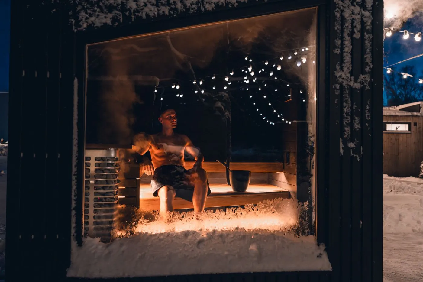A lit path to an outdoor sauna in the snow at night